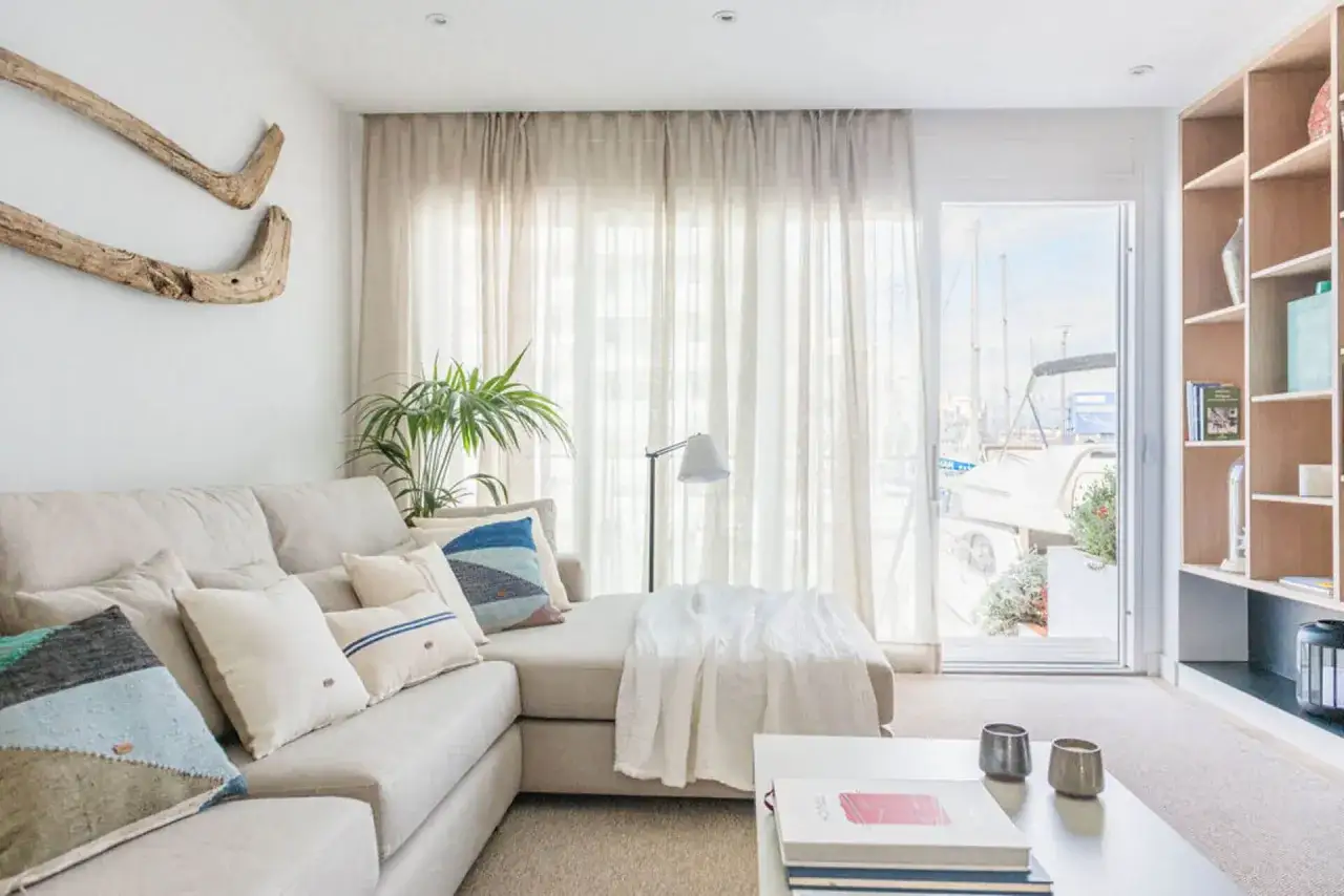 Sof&aacute; modular beige con chaise longue a la derecha, cojines coloridos, planta y vistas al puerto.