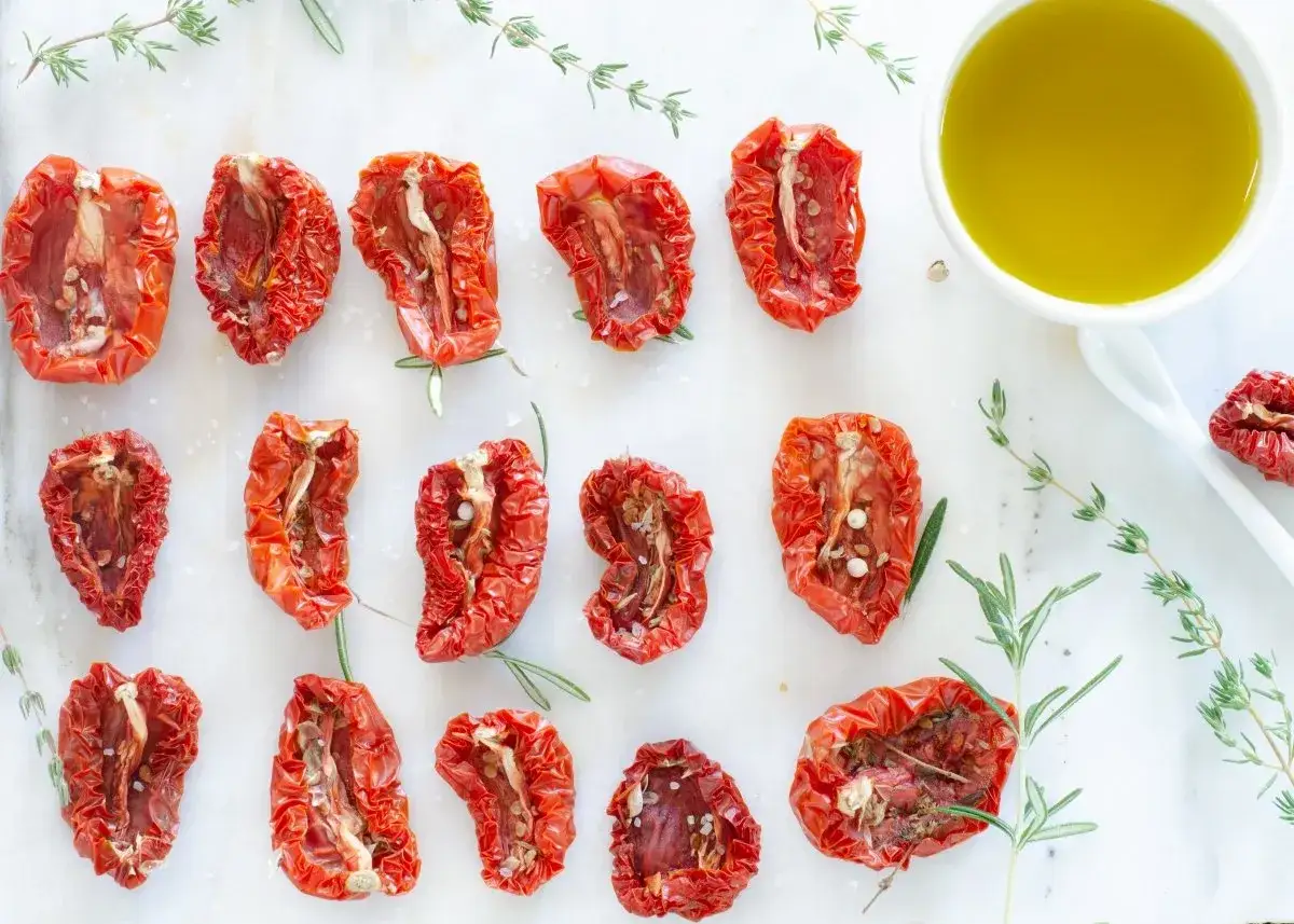 Tomates secos al horno, listos para usar en tus recetas. Aceite de oliva y hierbas frescas acompa&ntilde;an.
