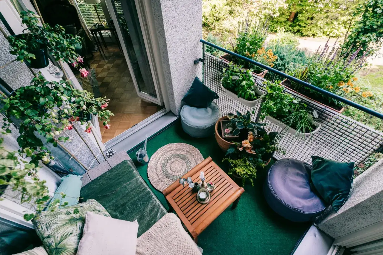 Grüner Teppich, Holzmöbel, Pflanzen und Kissen – tolle Balkon Ideen für eine gemütliche Oase.
