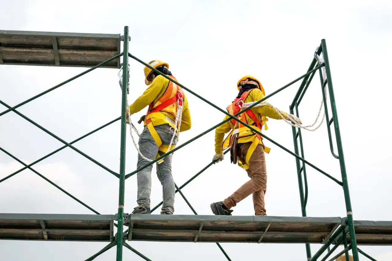Dos trabajadores con arneses de seguridad en andamios, mostrando diferentes tipos de andamios en construcción.
