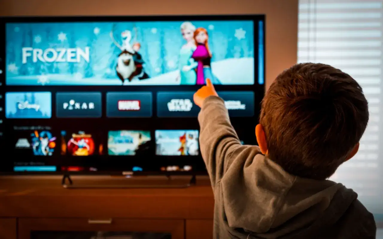 Chłopiec wskazuje palcem na ekran telewizora, gdzie wyświetlają się bajki Disneya dla 3 latka, w tym Kraina Lodu.