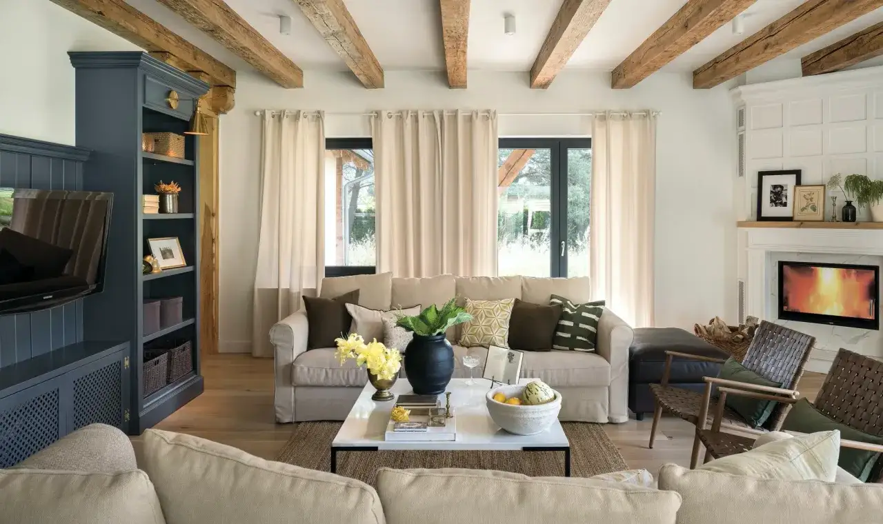 Przytulny salon w stylu farmhouse z widocznymi belkami stropowymi, kominkiem i wygodną kanapą.