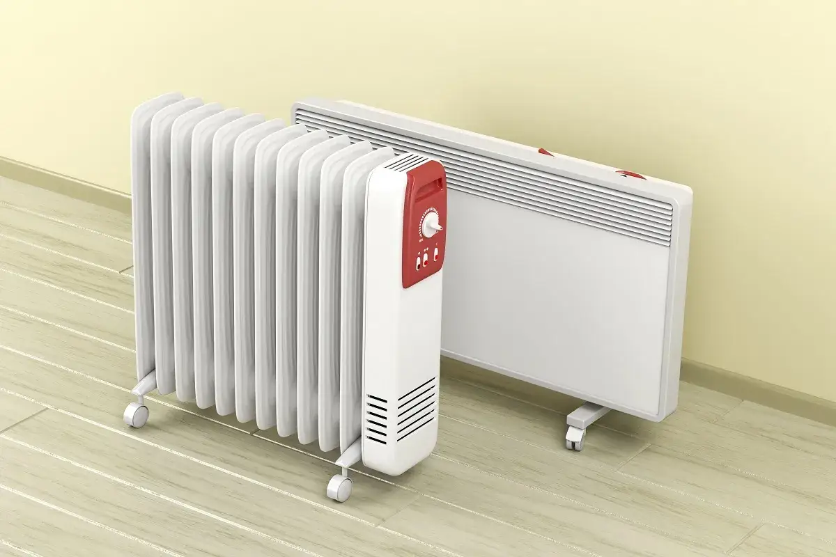 Dwa rodzaje grzejnik&oacute;w elektrycznych: olejowy z pokrętłem i panelowy. Oba białe, na k&oacute;łkach, stoją na drewnianej podłodze.