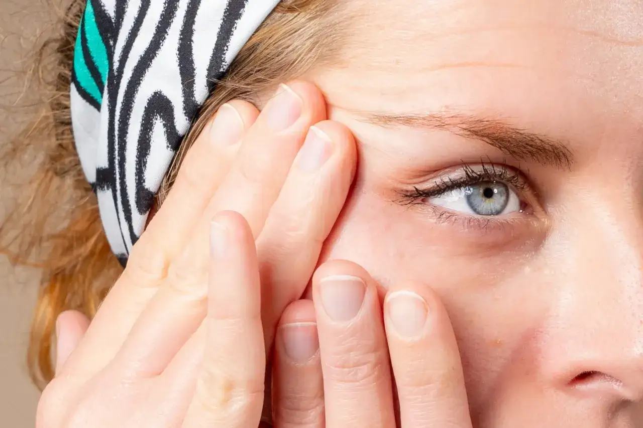 Doigts massant le contour de l'&oelig;il, une astuce pour enlever les poches sous les yeux naturellement. Bandeau &agrave; rayures noires et blanches.