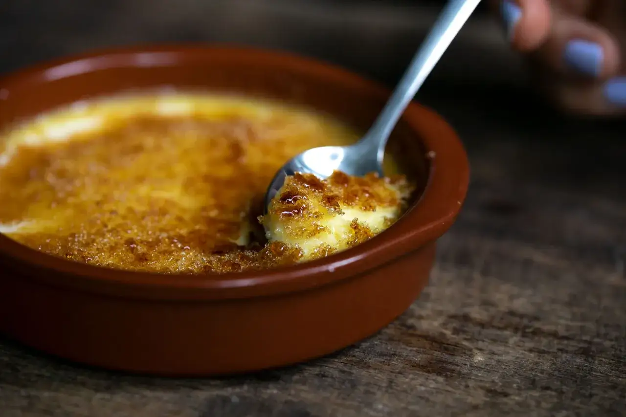 Creme brulee mit knuspriger Karamellkruste, die mit einem L&ouml;ffel angebrochen wird.