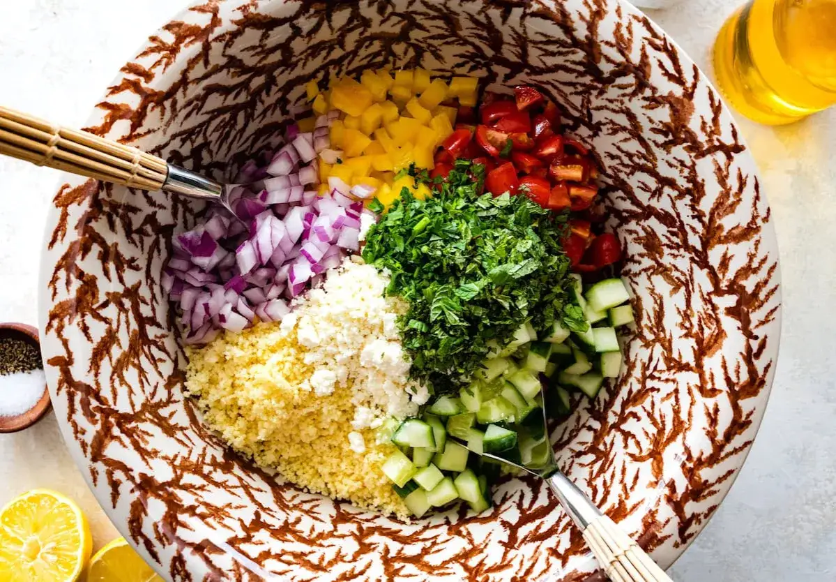 Bunte Zutaten für einen Couscous-Salat mit Feta: gewürfelte Tomaten, Gurken, rote Zwiebeln, gelbe Paprika, frische Kräuter und Feta.