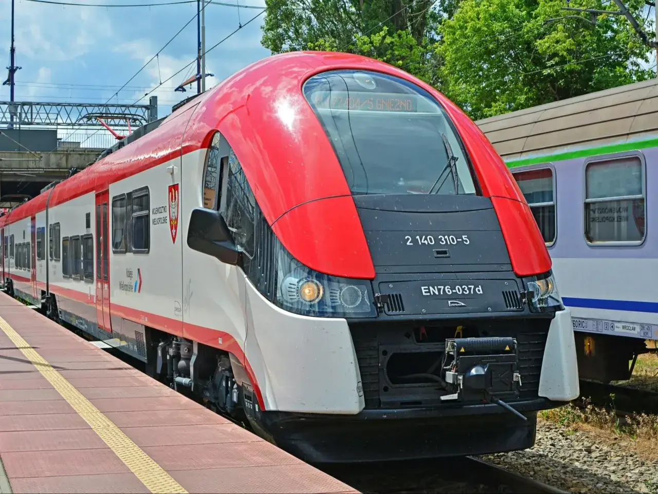 Czerwono-biały pociąg Kolei Wielkopolskich czeka na pasażer&oacute;w, by zabrać ich nad morze.