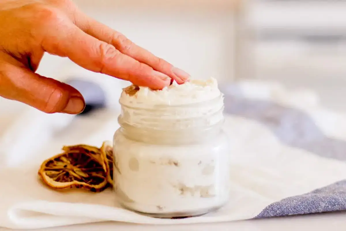 Handcreme selber machen f&uuml;r Kinder: Eine Hand taucht in ein Glas mit selbstgemachter Handcreme. Daneben liegen getrocknete Zitronenscheiben.