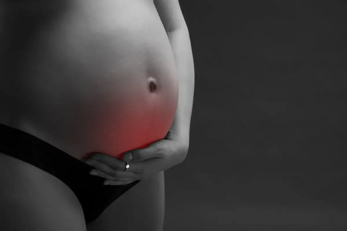 Ból brzucha w ciąży. Czy można brać Nospę? Kobieta trzyma dłońmi ciążowy brzuch, na którym zaznaczono czerwienią bolesne miejsce.