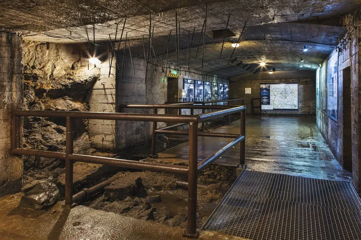 Wnętrze kompleksu rzeczka: betonowe ściany, mokra podłoga, metalowe balustrady i wystawy historyczne.