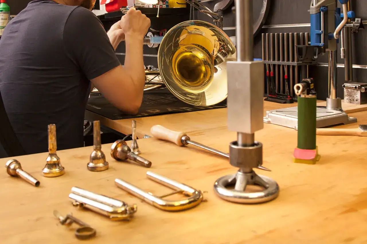 Werkstatt f&uuml;r Blasinstrumente Reparatur: Ein Mann arbeitet an einem goldenen Blasinstrument, Werkzeuge liegen bereit.