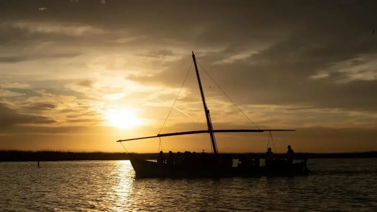 Un paseo en barca por la Albufera al atardecer, con el sol ti&ntilde;endo el cielo de oro y las siluetas de los viajeros reflej&aacute;ndose en el agua.