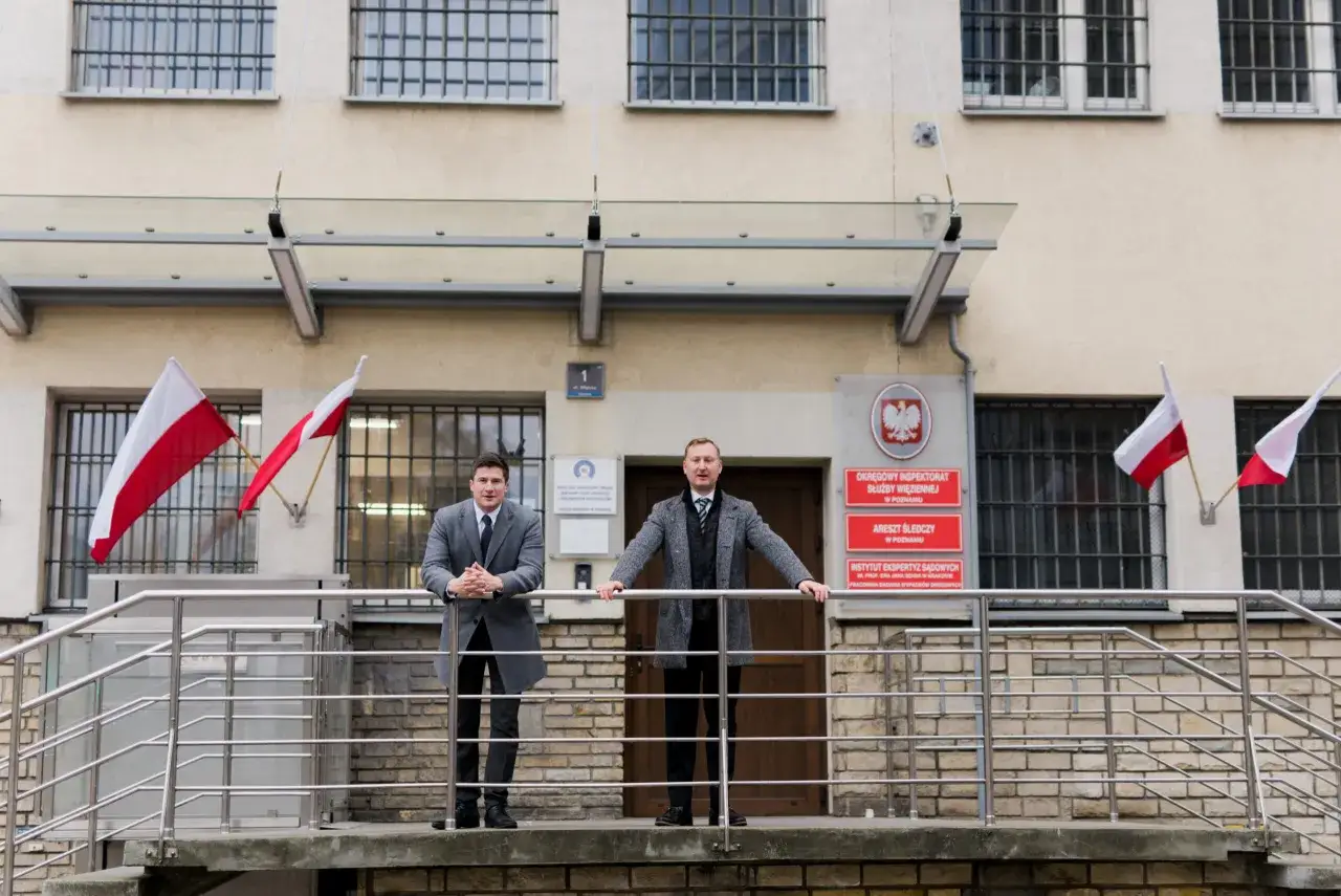 Dwóch mężczyzn w garniturach przed budynkiem z tablicami 