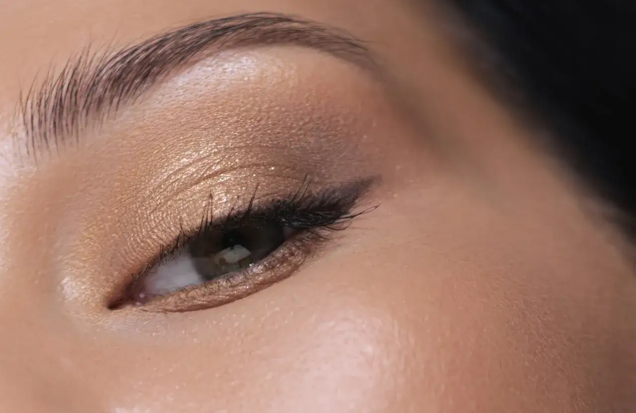 Maquillage paupi&egrave;re tombante : un fard dor&eacute; scintillant rehausse le regard, avec un trait d'eye-liner fin et des cils longs.