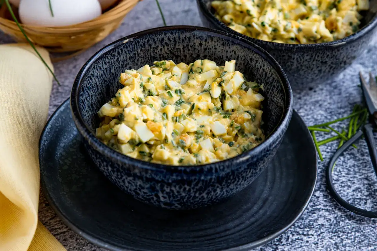 Ein cremiger eiersalat mit joghurt und frischen Kr&auml;utern, serviert in einer dunklen Sch&uuml;ssel.