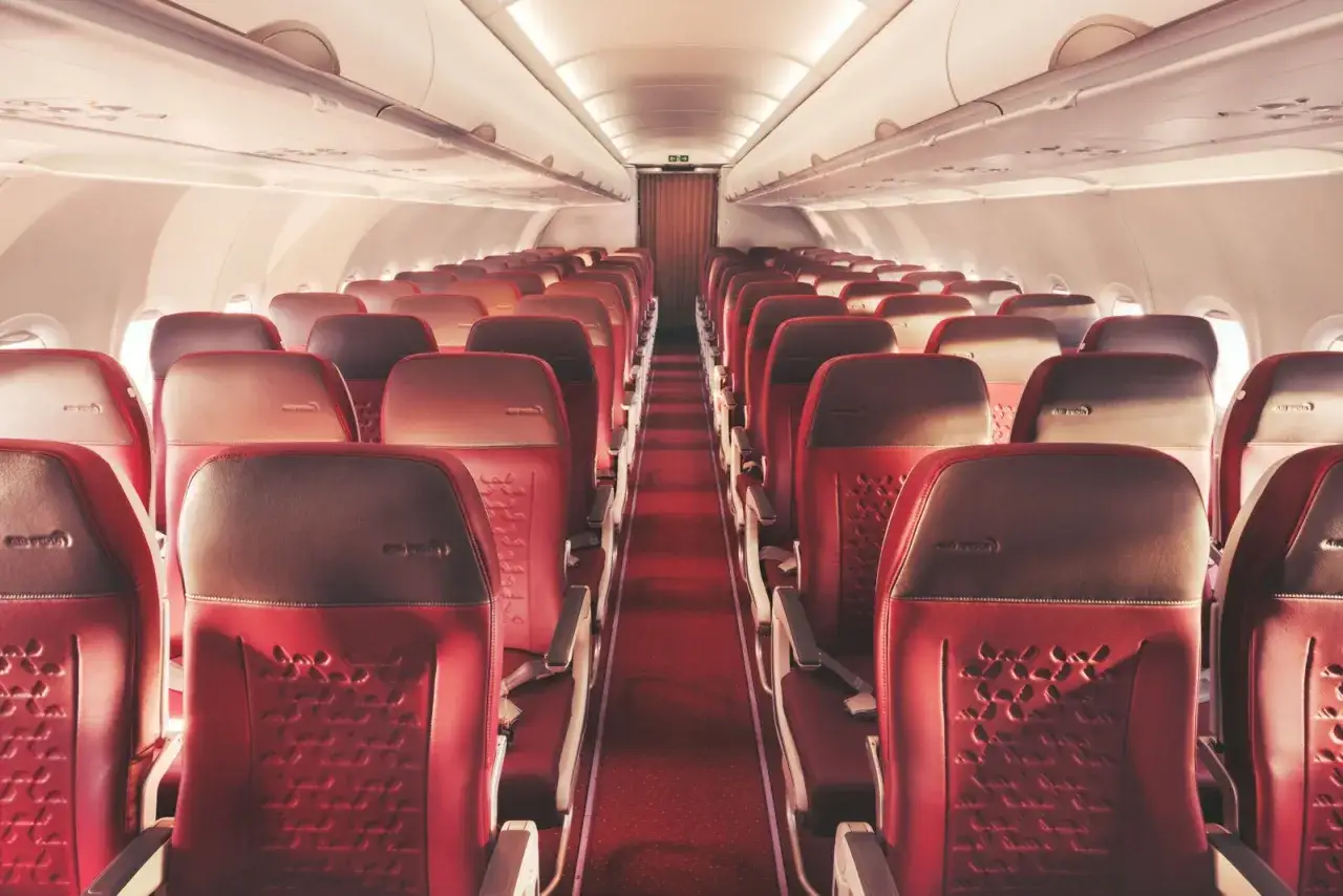Wnętrze samolotu A320neo z rzędami czerwonych, skórzanych foteli i dywanem w tym samym kolorze.