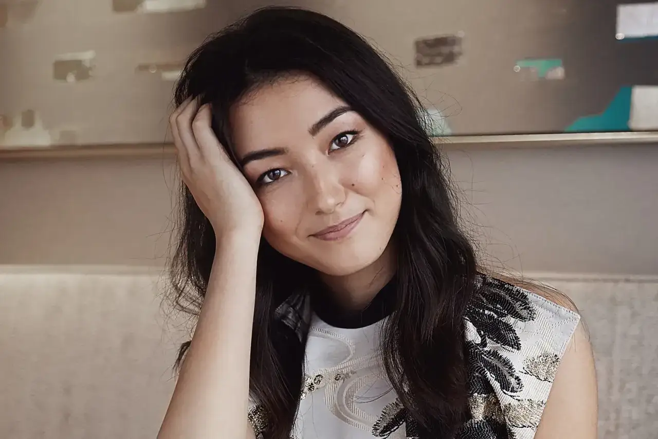 Natasha Liu Bordizzo ler mjukt med handen mot kinden, klädd i en mönstrad topp.