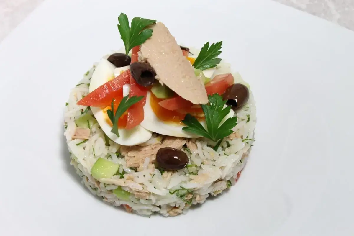 Une salade de riz gastronomique, garnie d'&oelig;ufs durs, tomates, olives, thon et persil, sur une assiette blanche.