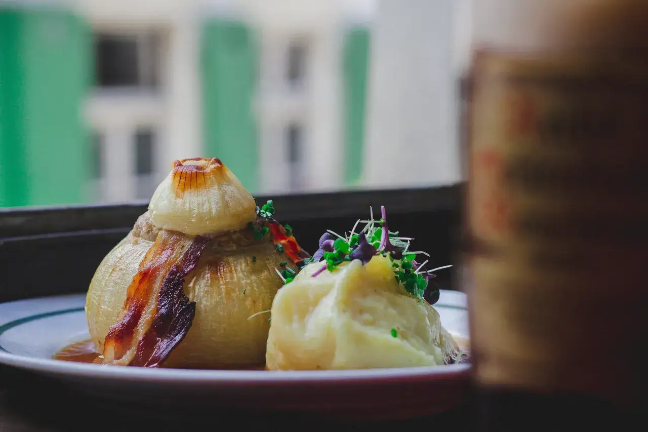 Gefüllte Bamberger Zwiebel mit Speck und Kartoffelpüree, garniert mit frischen Kräutern. Ein kulinarischer Genuss!