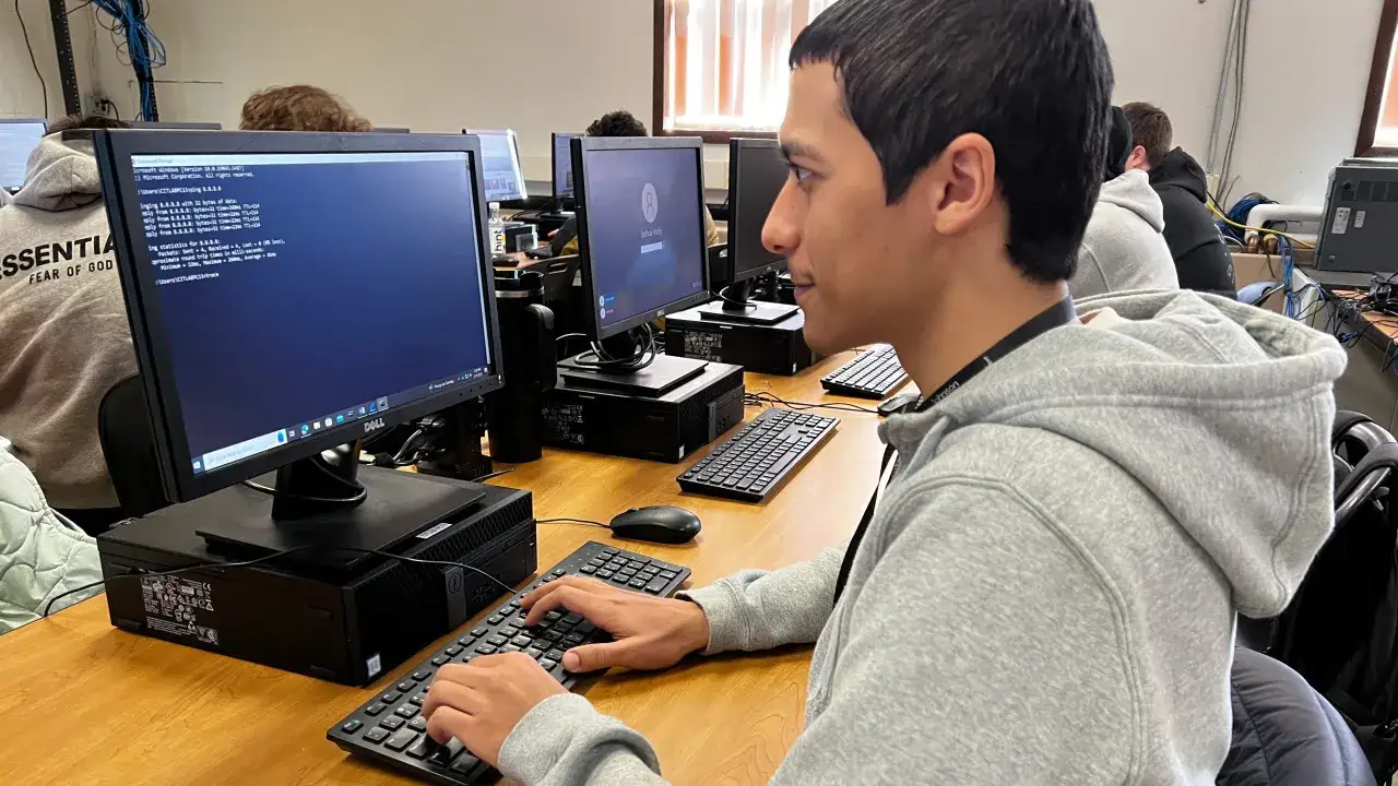 Un jeune homme concentr&eacute; sur son &eacute;cran, apprenant &agrave; ma&icirc;triser la cybers&eacute;curit&eacute; &agrave; distance. Il tape sur son clavier, analysant des donn&eacute;es r&eacute;seau.