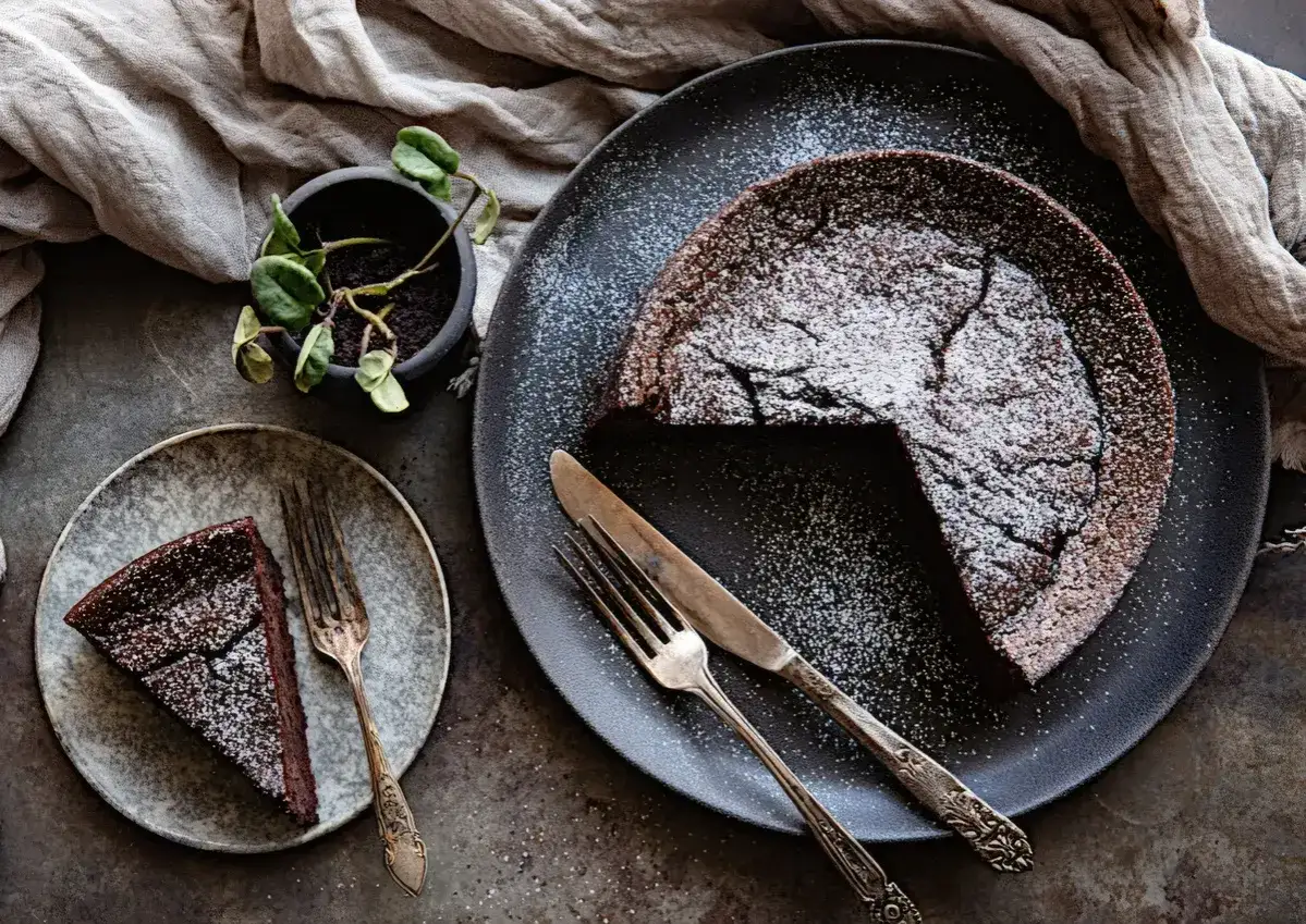Una fetta di torta tenerina, cosparsa di zucchero a velo, attende su un piatto, accanto a una torta intera.