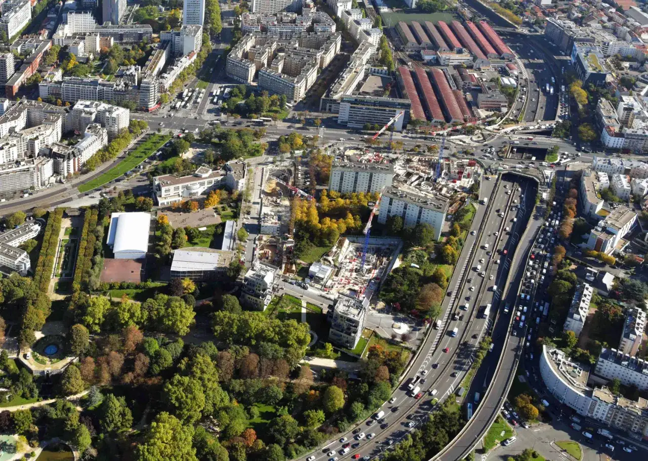 Vue a&eacute;rienne d'un chantier en cours sur le p&eacute;riph&eacute;rique parisien, entour&eacute; de b&acirc;timents r&eacute;sidentiels et d'espaces verts.