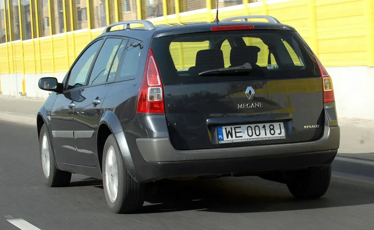 Ciemnoszary Renault Megane 2 kombi jedzie po drodze, za żółtą barierą dźwiękochłonną.