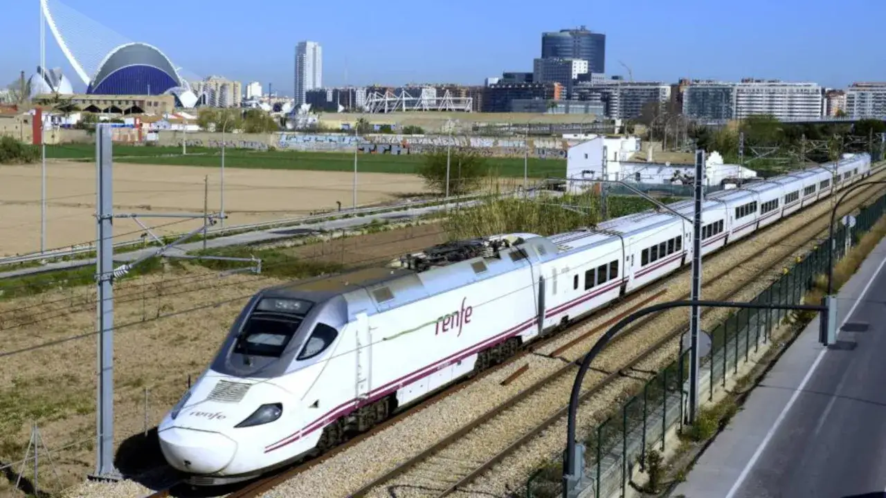 Tren Renfe blanco y morado en v&iacute;as, con edificios modernos y un puente ic&oacute;nico al fondo. Viaje r&aacute;pido de Madrid a Castell&oacute;n.