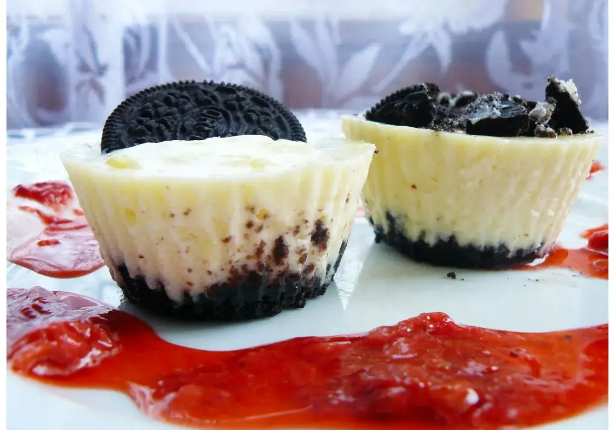 Mini serniczki Oreo z polewą truskawkową. Pyszne, kremowe desery z ciasteczkowym spodem i kawałkami Oreo.