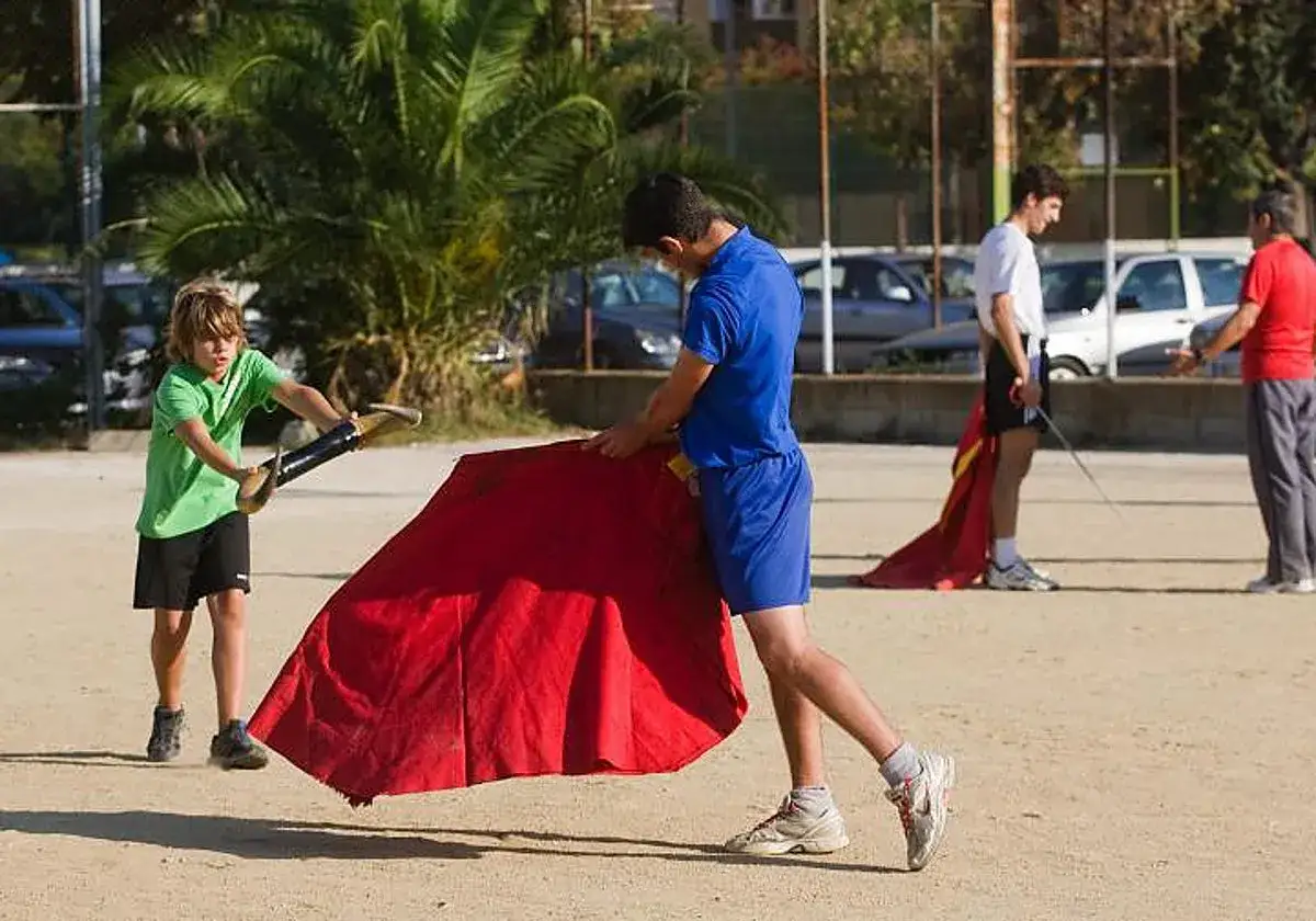 J&oacute;venes aprenden a torear con capotes rojos en un ruedo.