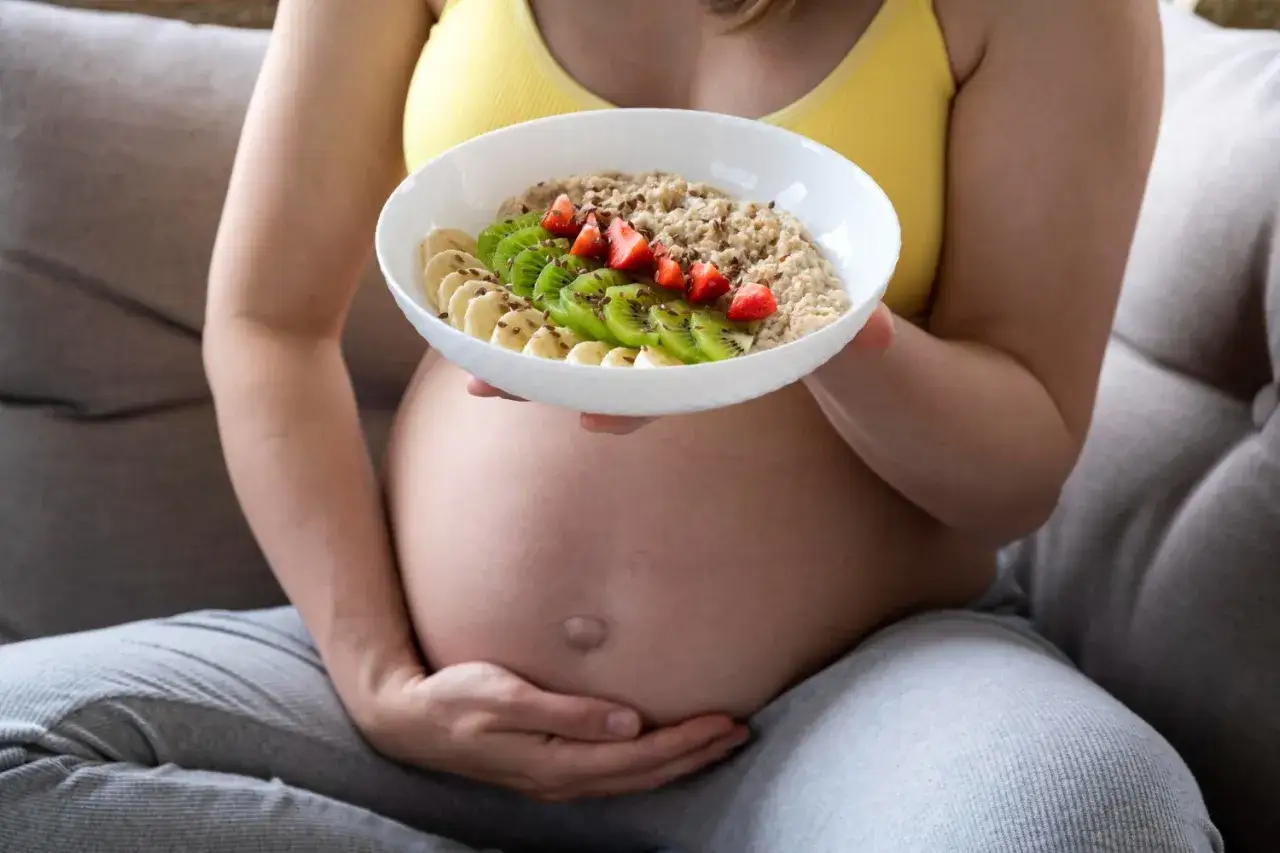 Kobieta w ciąży z miską owsianki z owocami, dbająca o dietę, by zapobiec anemii w ciąży.