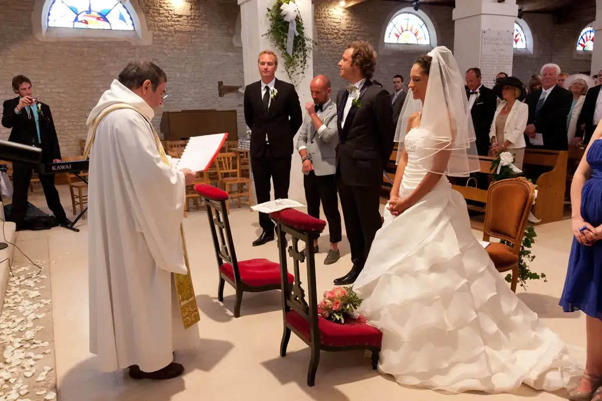 C&eacute;r&eacute;monie de mariage : le pr&ecirc;tre lit la pri&egrave;re des &eacute;poux devant la mari&eacute;e en robe blanche et le mari&eacute;.