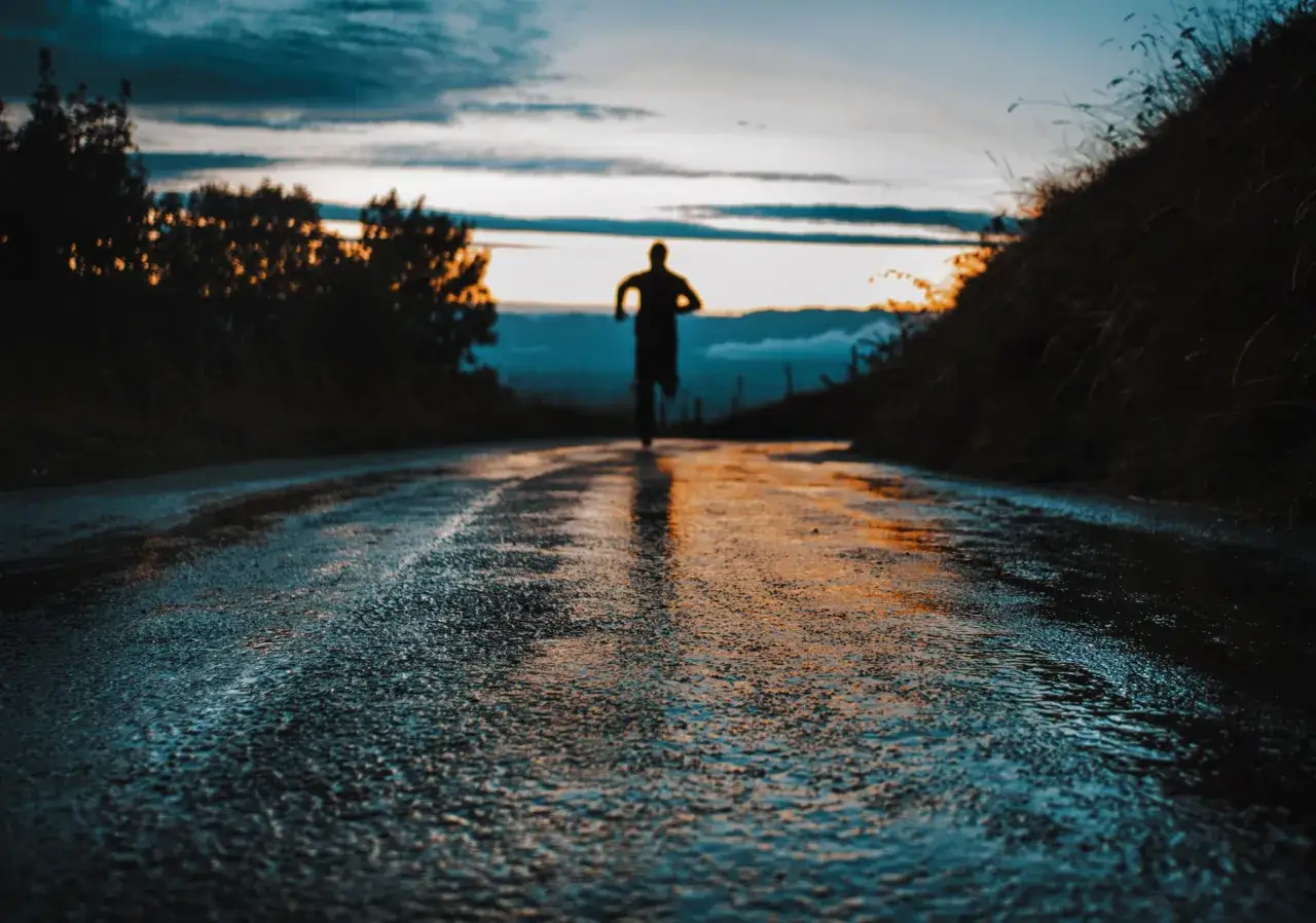 Un corridore solitario all'alba, con la strada bagnata che riflette i colori del cielo. Un'ispirazione per la tabella maratona 3 ore 30.