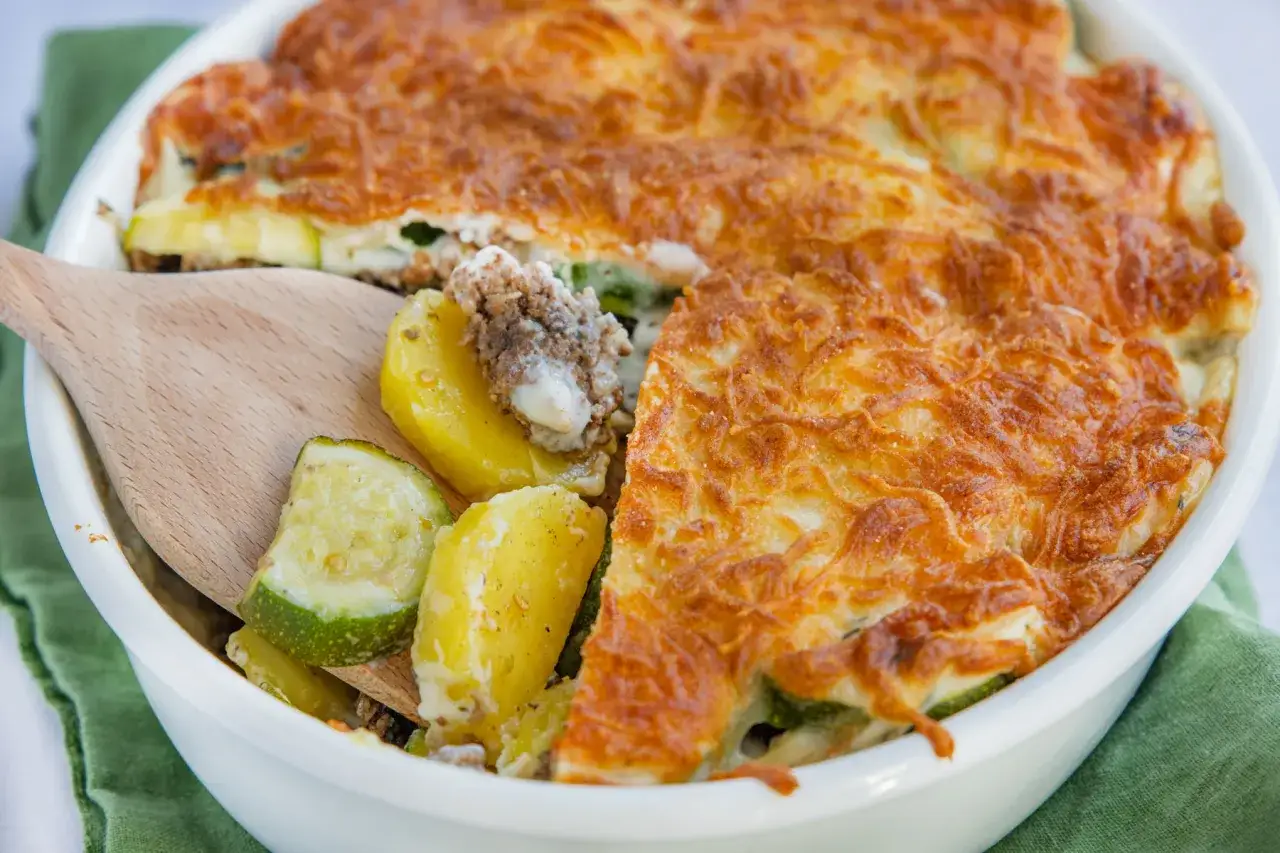 Ein goldbraun überbackener Zucchini Auflauf mit Kartoffeln und Hackfleisch, bereit zum Servieren.