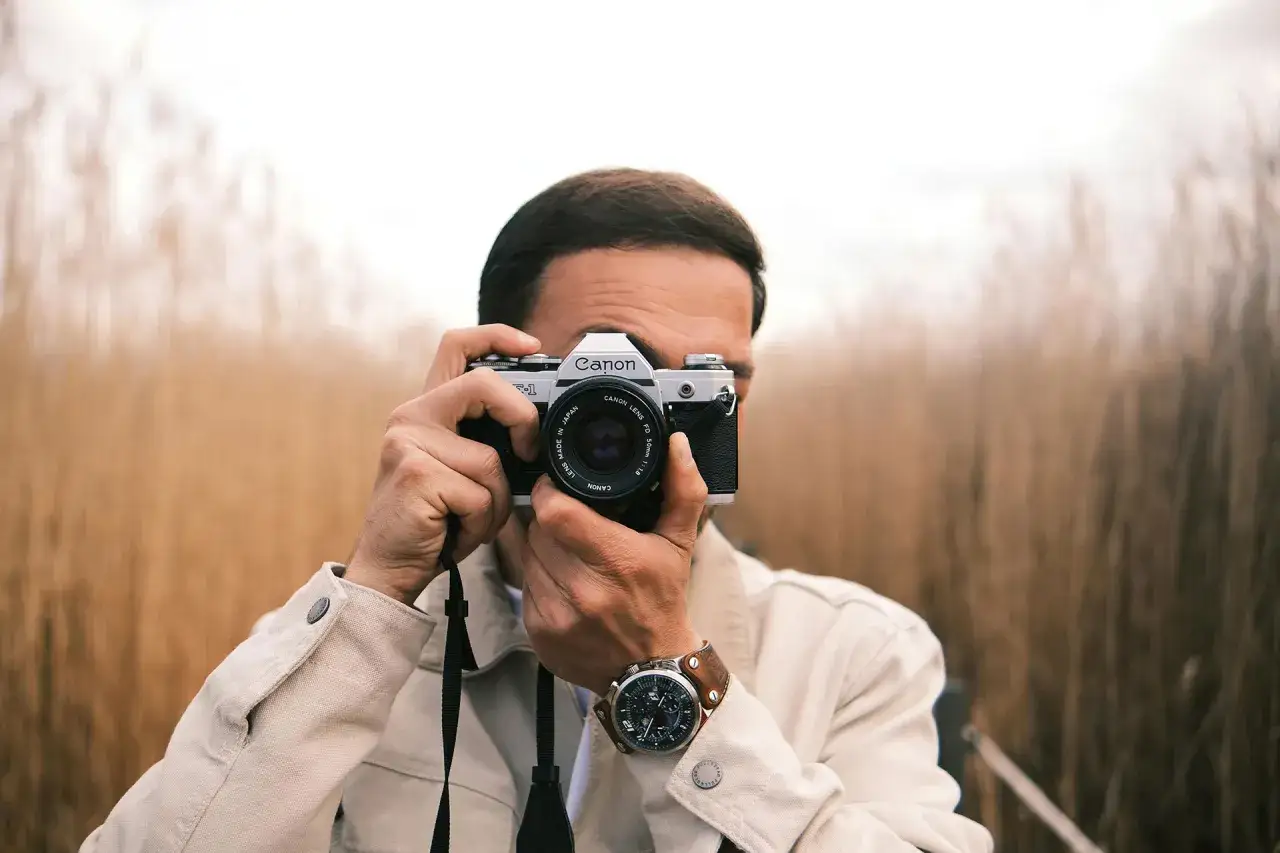 Man with a Canon AE-1, a classic choice for the best film camera for street photography, captures the moment amidst a field of tall grass.