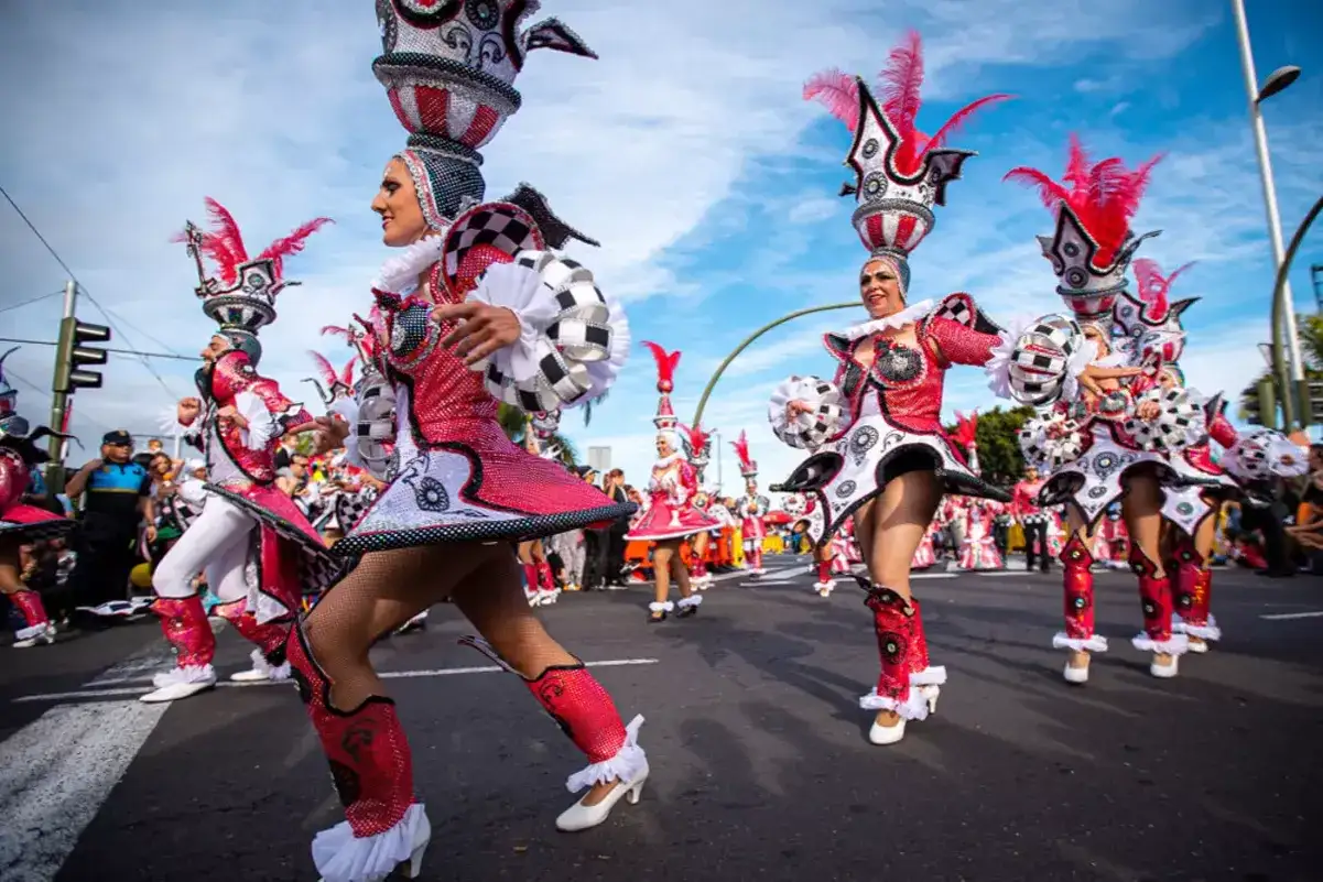 Desfile de carnaval con bailarines en trajes brillantes y elaborados sombreros. ¡Un destino ideal donde viajar en febrero para vivir esta fiesta!