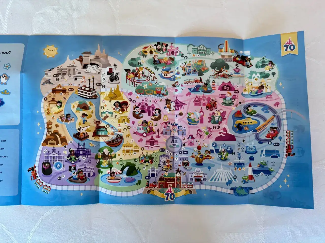 Kolorowa mapa atrakcji Disneyland, gdzie jest pełno postaci z bajek i miejsc do zabawy.
