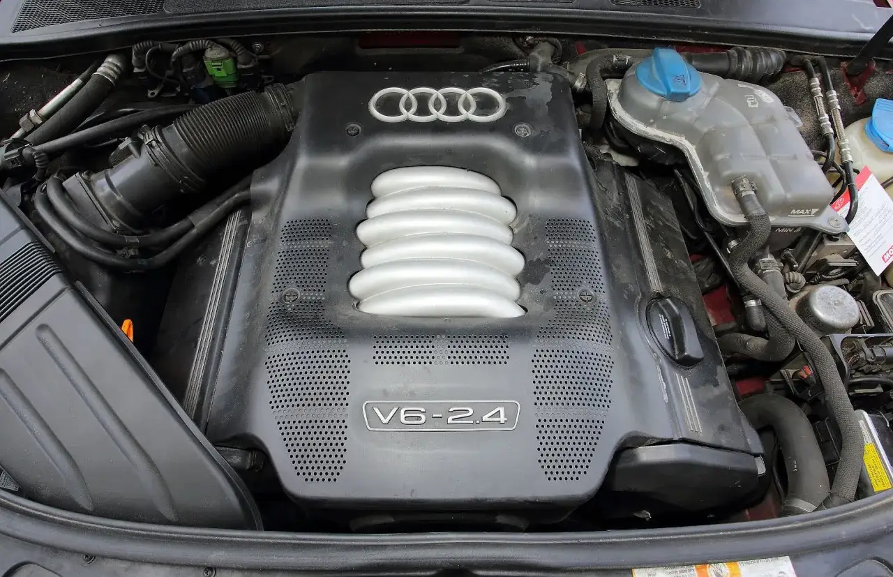 Silnik V6 2.4 benzyna w Audi A4 B6. Widoczny kolektor dolotowy i osłona silnika z logo Audi.