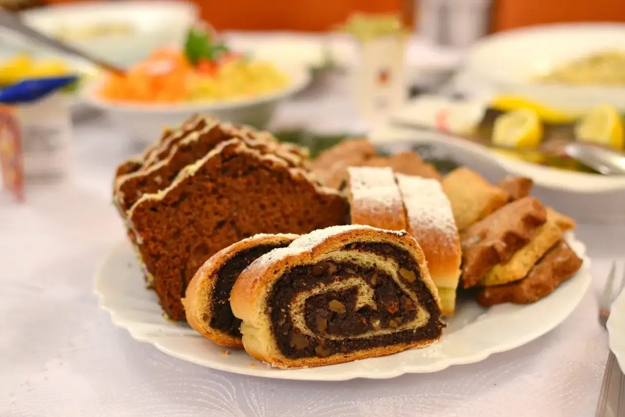 Stary przepis babci na makowiec, pachnący domem i świętami. Na talerzu obok ciasta z makiem, kawałki piernika i inne słodkości.