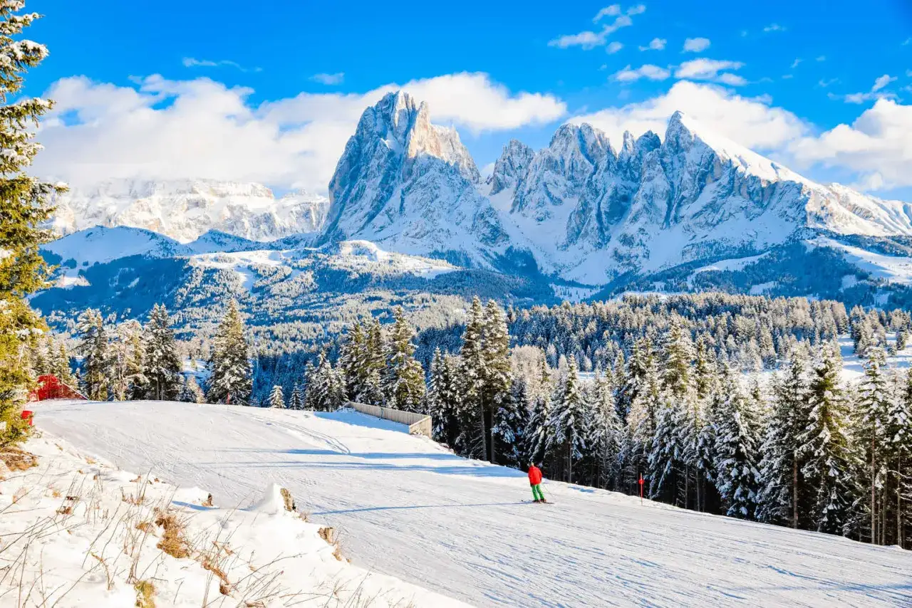 Słoneczny dzień na stoku narciarskim w Dolomitach. Jeden narciarz zjeżdża po ośnieżonej trasie, w tle majestatyczne, ośnieżone szczyty. Idealne regiony narciarskie Włoch.