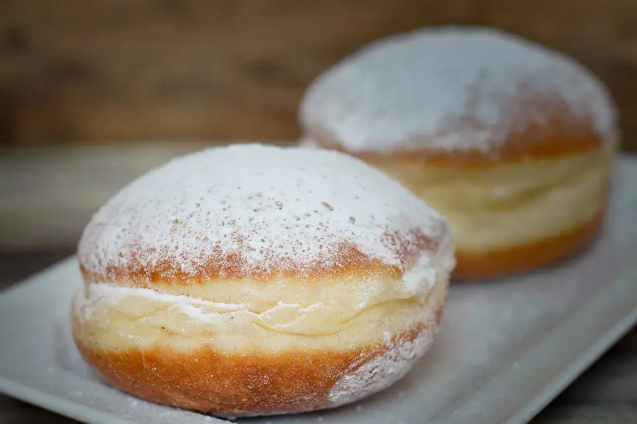 Dwa pączki posypane cukrem pudrem. Czy pączki są wegańskie? Trudno powiedzieć, wyglądają apetycznie.