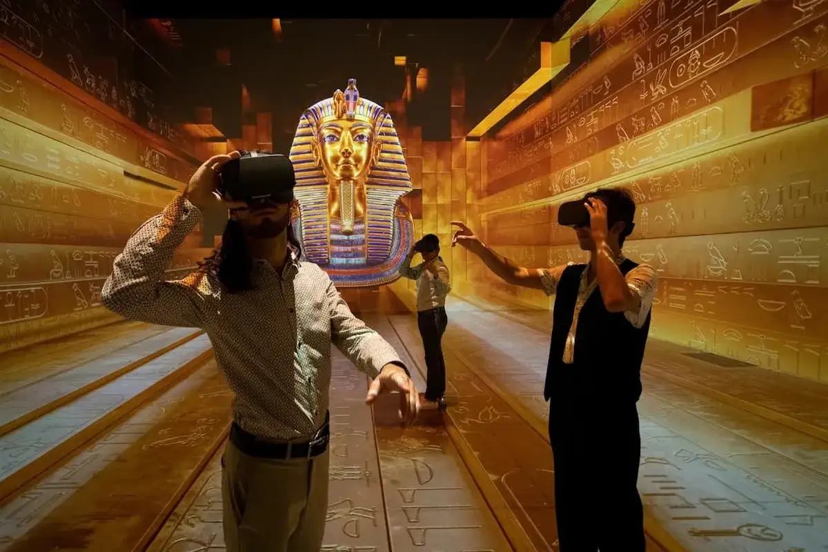 Upplev forntida Egypten i ett 3D museum i Stockholm. Besökare med VR-glasögon utforskar en gyllene gravkammare med Tutankhamons mask.