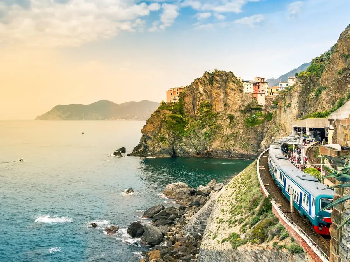 Mit dem Zug ans Meer Italien: Ein Zug fährt entlang der felsigen Küste Italiens, vorbei an bunten Häusern und dem türkisfarbenen Meer.