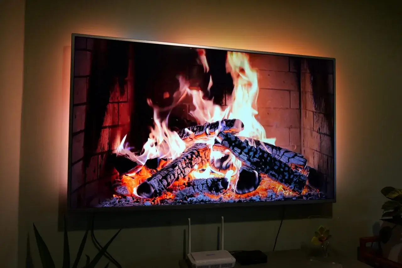 Aplikacja kominek w telewizorze tworzy przytulną atmosferę. Płonące polana w ceglanym palenisku rozświetlają ekran.