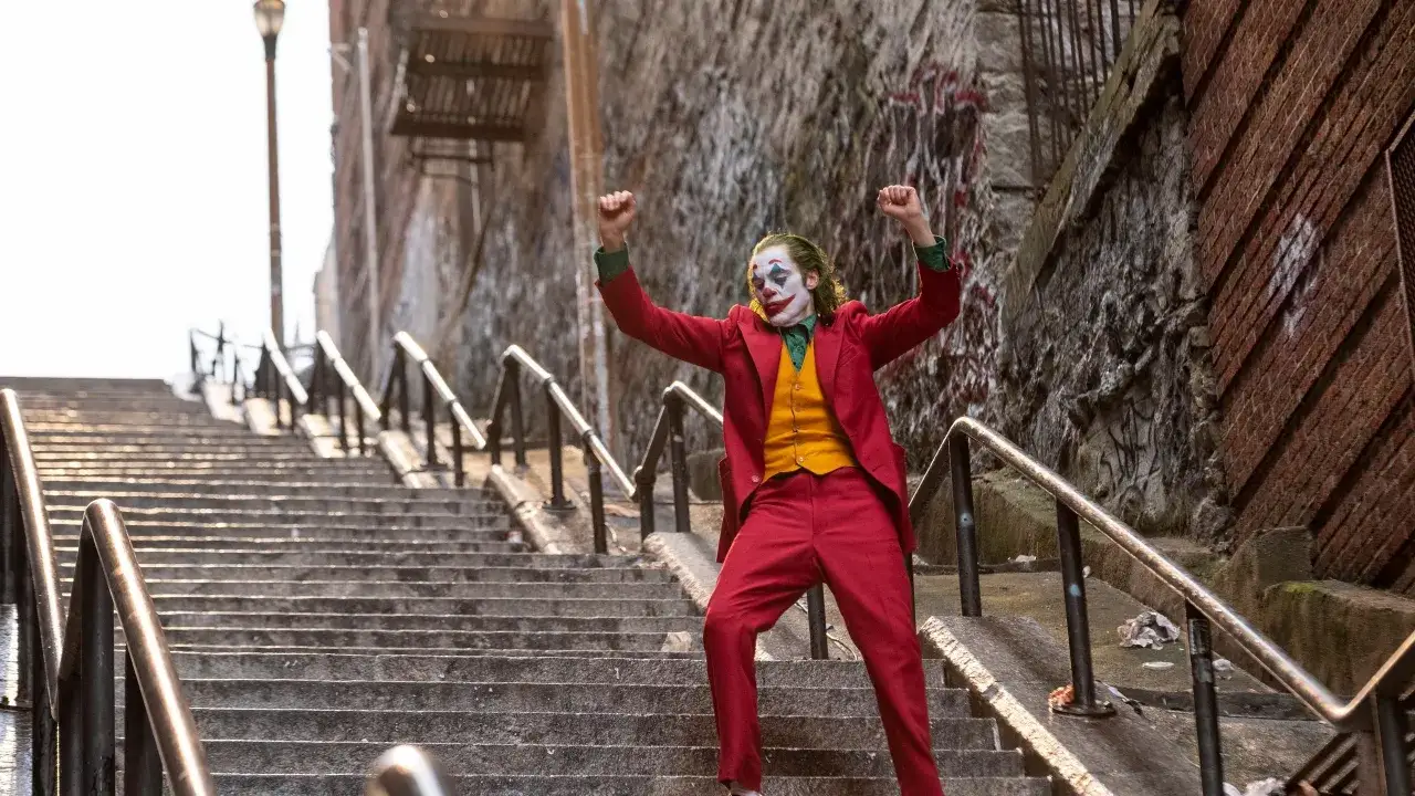 Joker, con trucco e abito rosso, balla sulle scale, un momento iconico della trama del film.