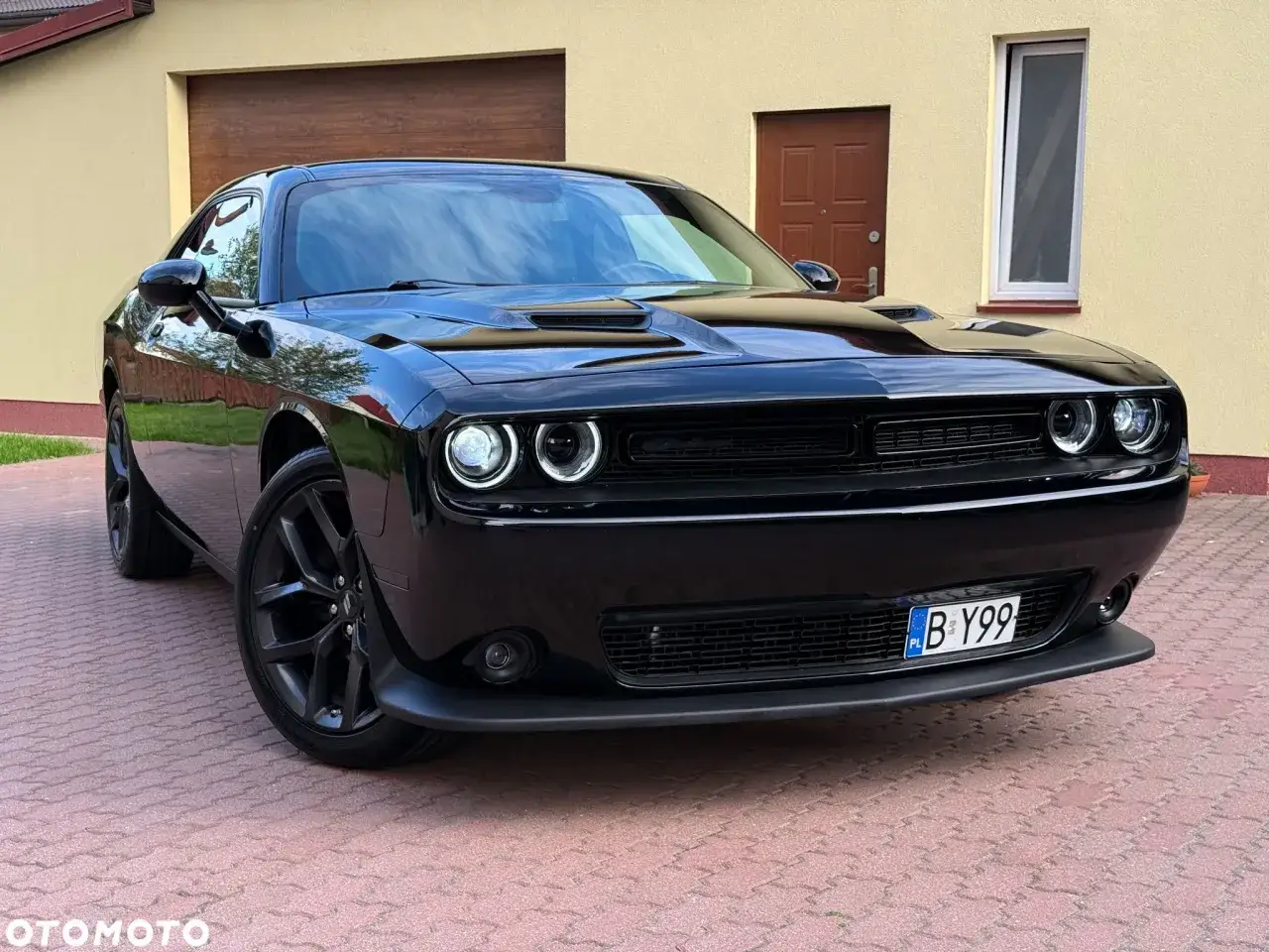 Czarny Dodge Challenger na podjeździe. Sprawdź atrakcyjną dodge challenger cena i poczuj moc amerykańskiego muscle cara.