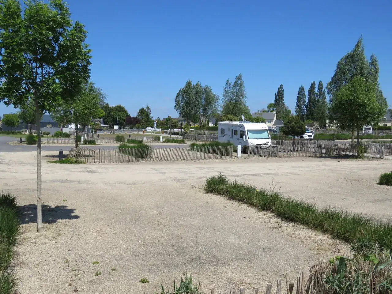 Un camping-car blanc est garé dans un camping en Normandie, sous un ciel bleu éclatant.