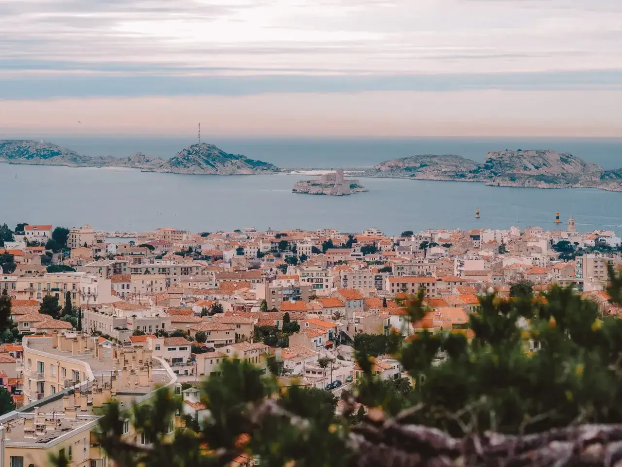 Widok na miasto z dachami i morzem w tle, z widocznym zamkiem na wyspie. To piękne **Marseille**.