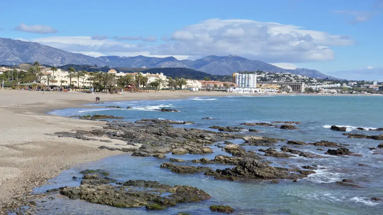 Felsige K&uuml;ste und Sandstrand der playa de calahonda mit Hotels und Bergen im Hintergrund.