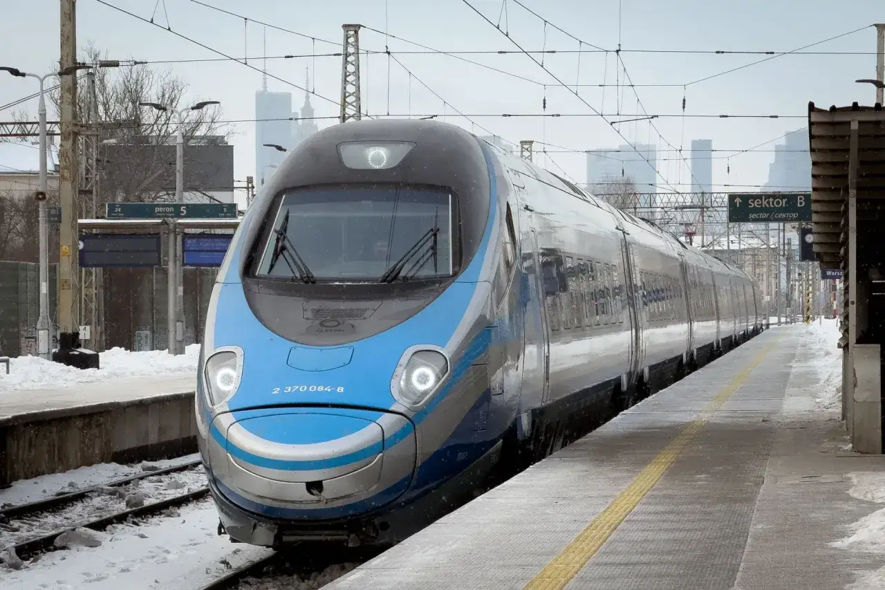 Pendolino w zimowej scenerii na dworcu. Pociąg PKP Intercity z niebiesko-srebrnym malowaniem stoi na torach, w tle widać miejską panoramę.